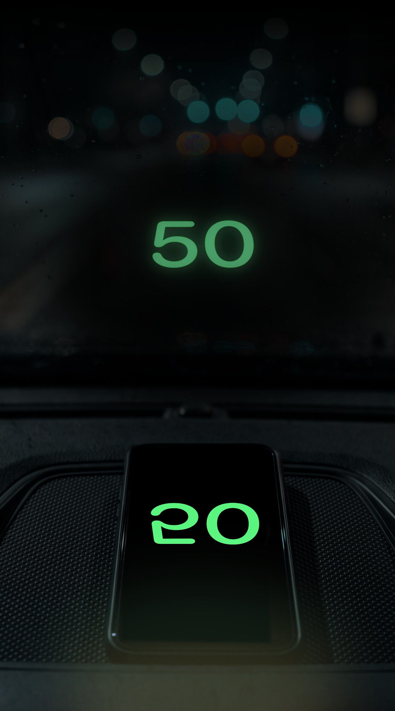 A phone on the dashboard showing a mirrored green 50, reflected the right way round on the windshield at night